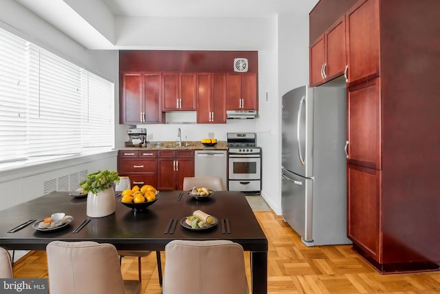 kitchen with appliances with stainless steel finishes, dark brown cabinets, under cabinet range hood, and a sink