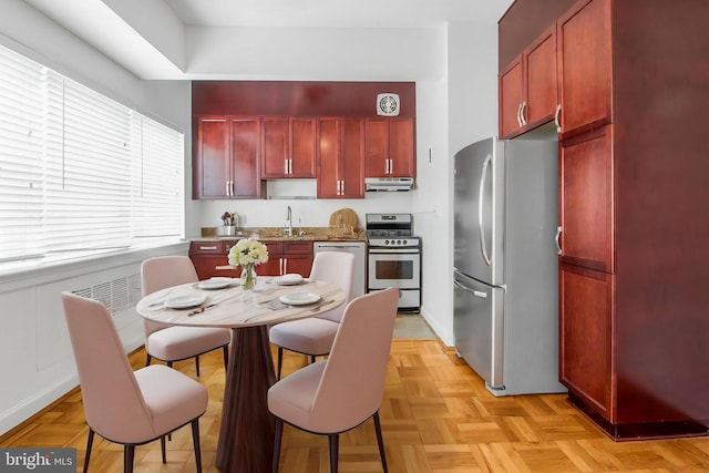 kitchen with appliances with stainless steel finishes, reddish brown cabinets, under cabinet range hood, and a sink