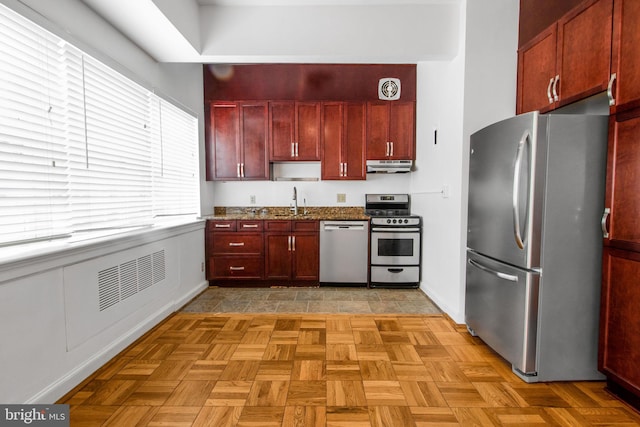 kitchen with stainless steel appliances, under cabinet range hood, dark brown cabinets, a sink, and baseboards