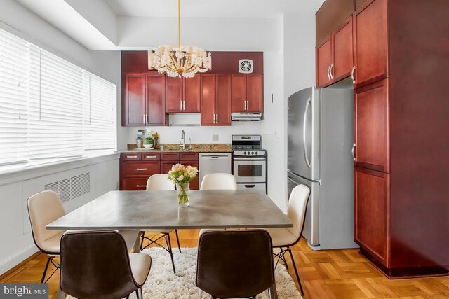 kitchen featuring stainless steel appliances, reddish brown cabinets, under cabinet range hood, a sink, and a chandelier
