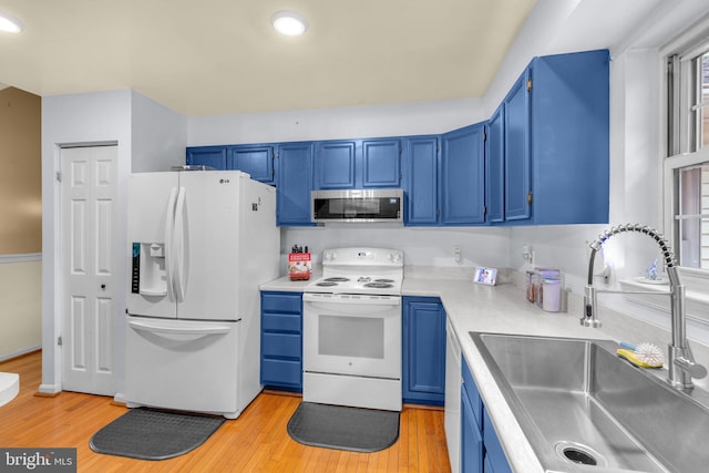 kitchen featuring white appliances, a sink, blue cabinets, light wood finished floors, and recessed lighting