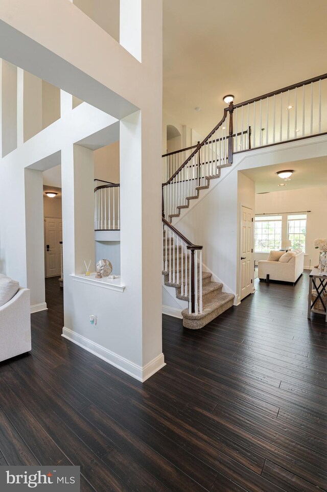 unfurnished living room featuring a towering ceiling, stairway, hardwood / wood-style flooring, and baseboards