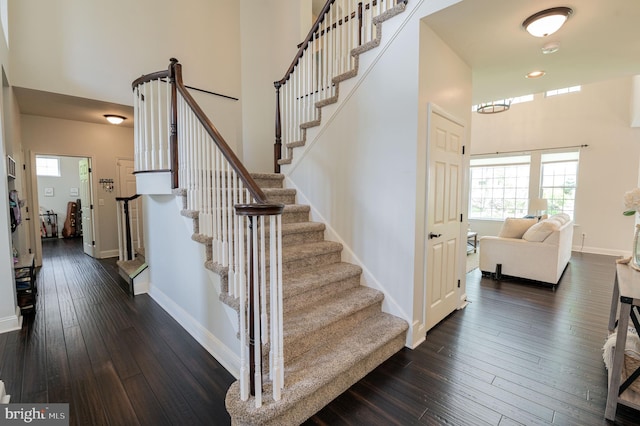 staircase featuring hardwood / wood-style floors, plenty of natural light, baseboards, and a high ceiling