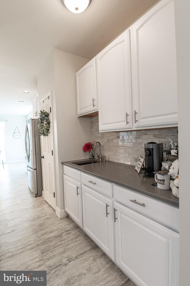 kitchen with freestanding refrigerator, a sink, dark countertops, light wood-style floors, and tasteful backsplash
