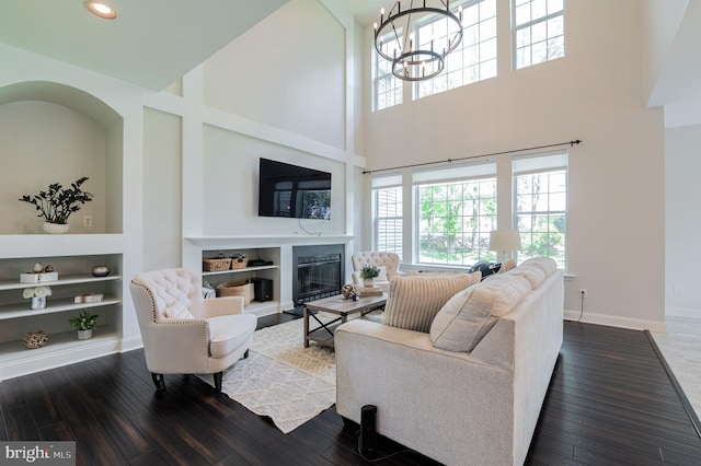 living area featuring a towering ceiling, wood-type flooring, a glass covered fireplace, healthy amount of natural light, and built in shelves