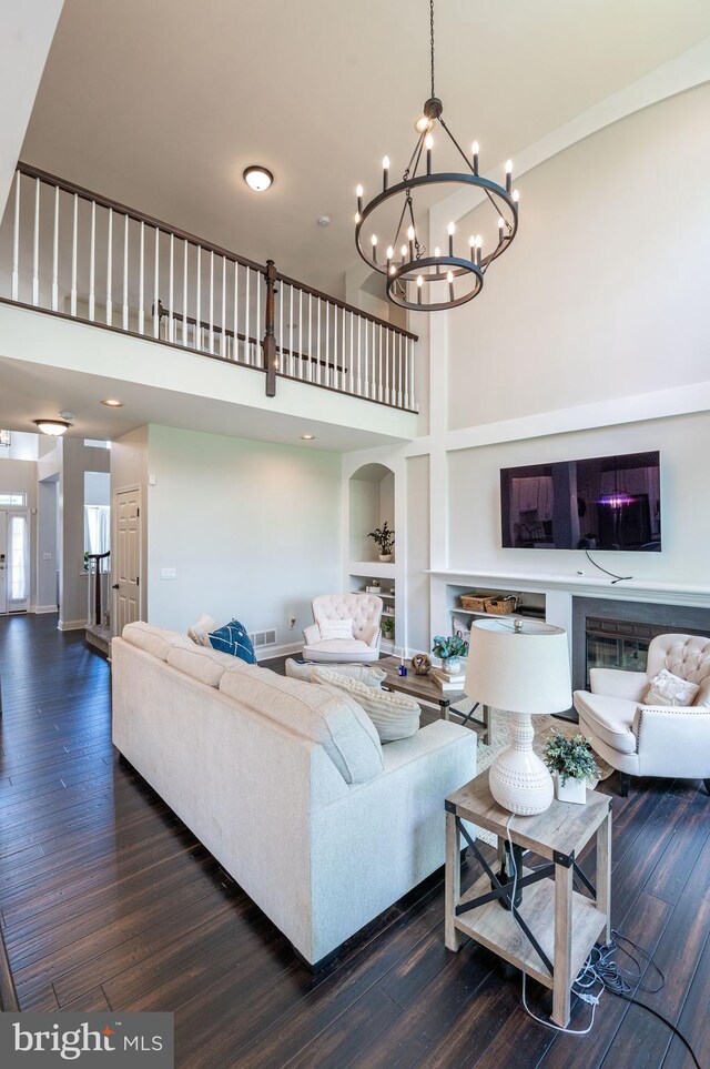 living room with a high ceiling, wood finished floors, built in shelves, and a chandelier