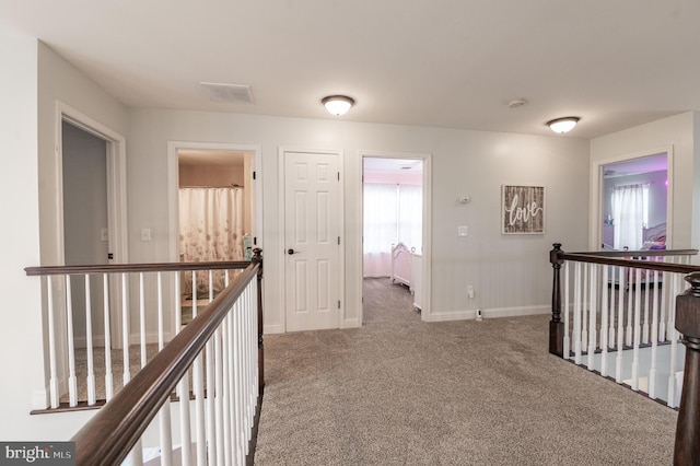 hall with an upstairs landing, carpet flooring, and baseboards