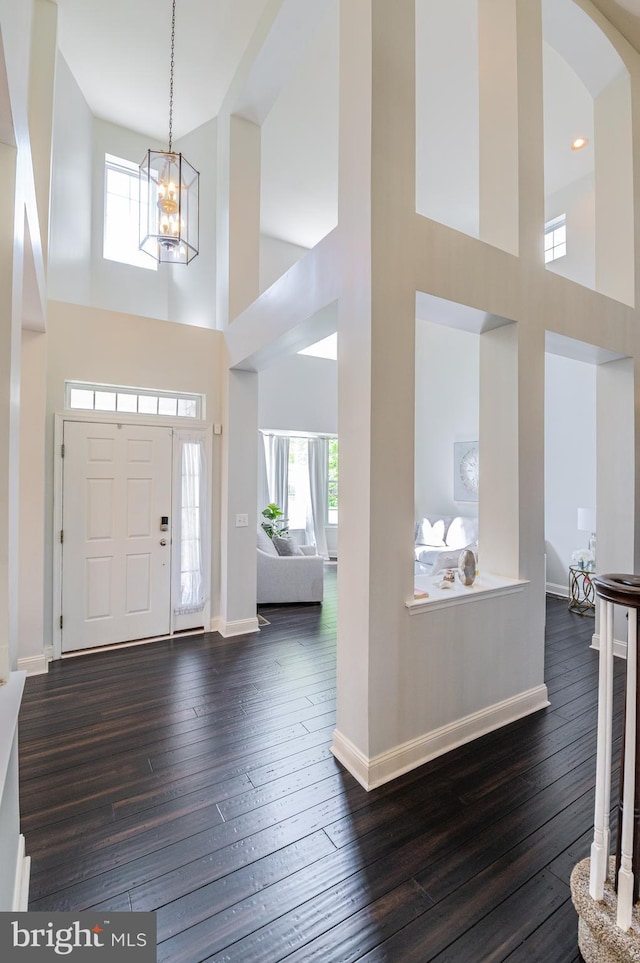 foyer featuring a towering ceiling, a chandelier, healthy amount of natural light, dark wood-type flooring, and baseboards