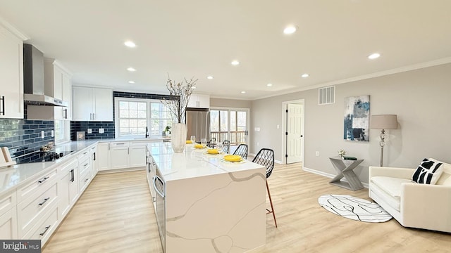 kitchen with wall chimney exhaust hood, a center island, crown molding, a breakfast bar, and black electric cooktop