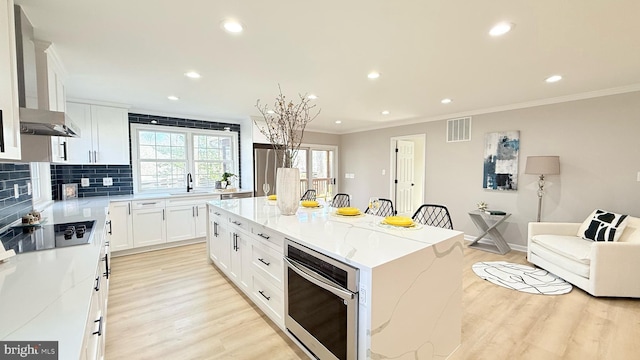 kitchen with black electric stovetop, a sink, light wood-type flooring, ornamental molding, and light stone countertops