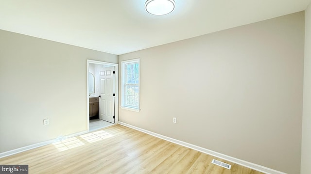 unfurnished bedroom with baseboards, light wood-type flooring, and ensuite bath