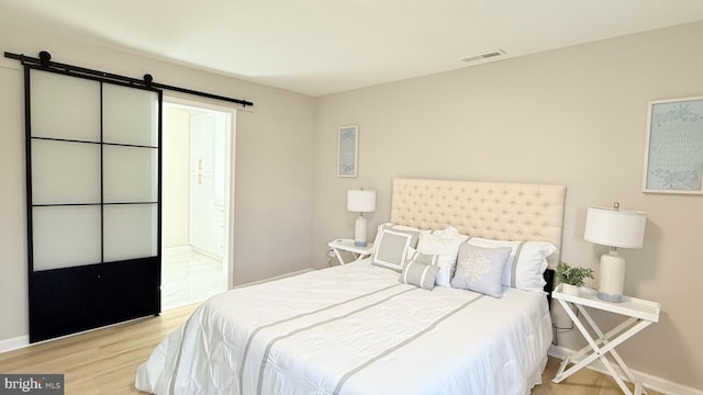 bedroom with a barn door, wood finished floors, and baseboards
