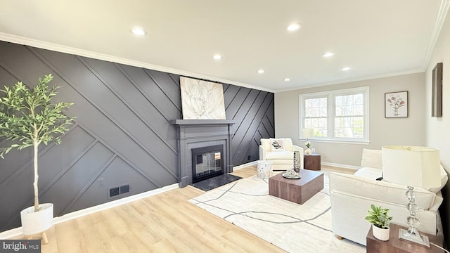 living room with a decorative wall, crown molding, wood finished floors, recessed lighting, and baseboards