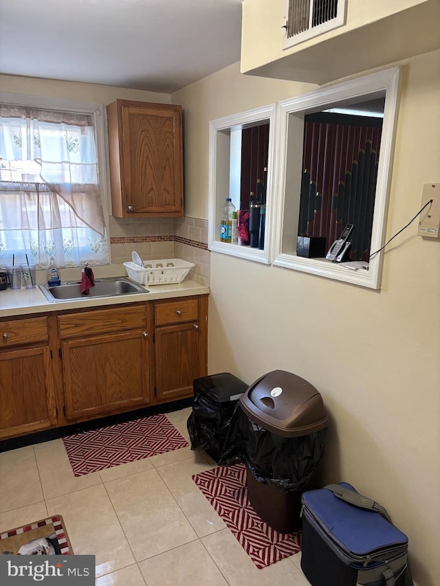 kitchen with brown cabinetry, a sink, light countertops, light tile patterned floors, and tasteful backsplash