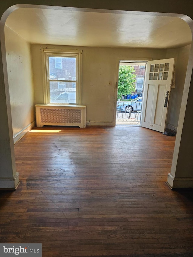 unfurnished room with arched walkways, radiator heating unit, and wood-type flooring