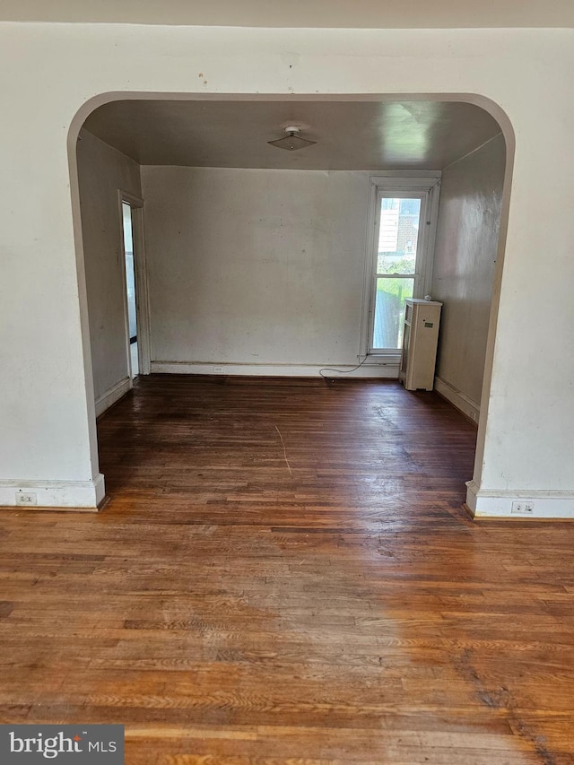 unfurnished dining area with arched walkways and wood finished floors