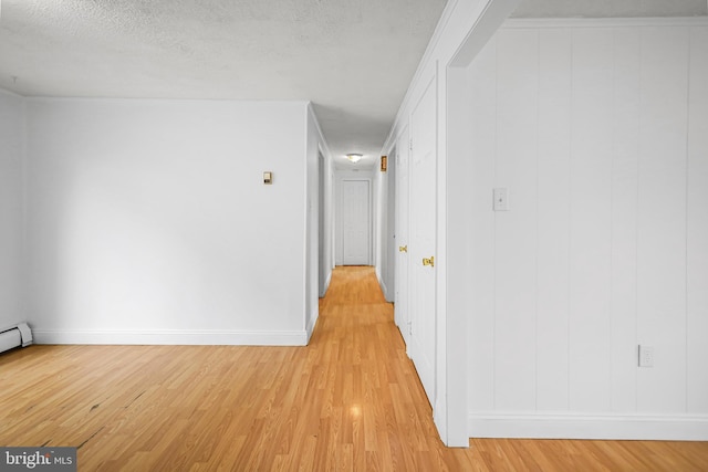 hallway featuring light wood-type flooring, baseboards, and a textured ceiling