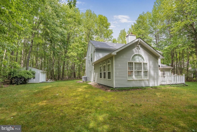 view of side of home featuring central AC unit, a chimney, an outbuilding, and a lawn