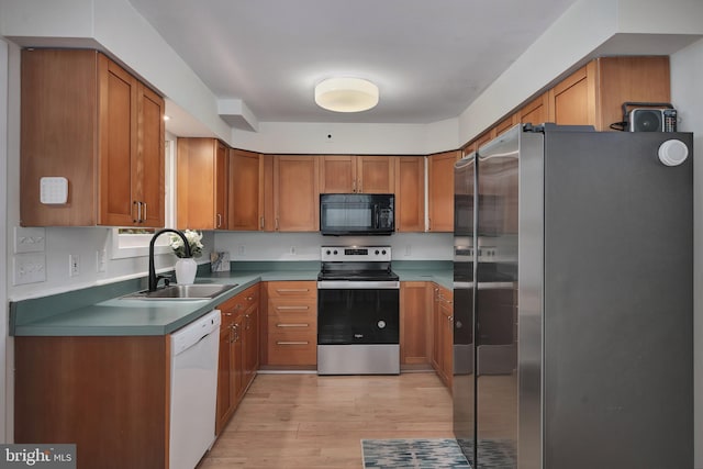 kitchen with appliances with stainless steel finishes, a sink, light wood-type flooring, and brown cabinetry