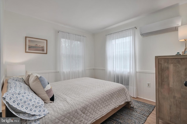 bedroom featuring a wall unit AC, a wainscoted wall, and wood finished floors