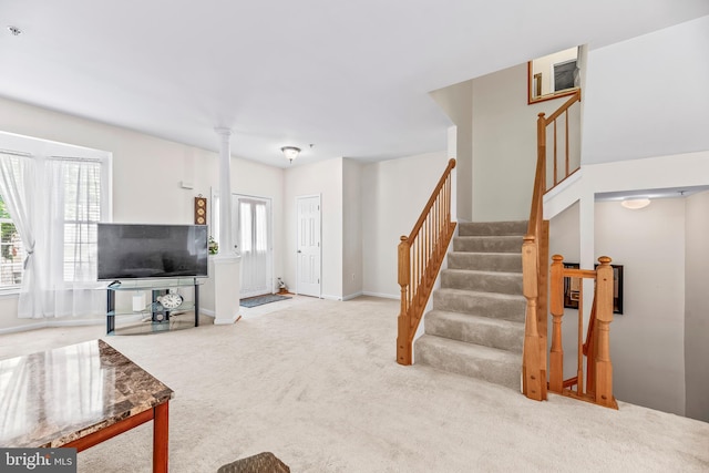 carpeted living room featuring stairway, baseboards, and decorative columns