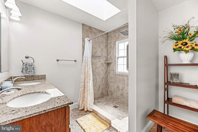bathroom with a skylight, tiled shower, baseboards, and double vanity