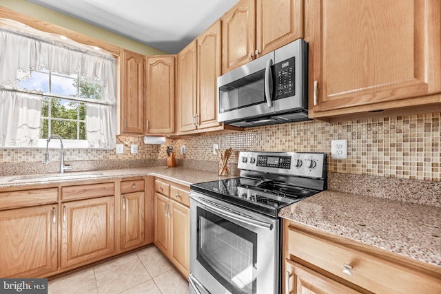 kitchen with stainless steel appliances, a sink, light brown cabinetry, tasteful backsplash, and light tile patterned floors