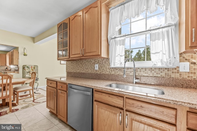kitchen featuring stainless steel dishwasher, backsplash, a sink, glass insert cabinets, and light stone countertops
