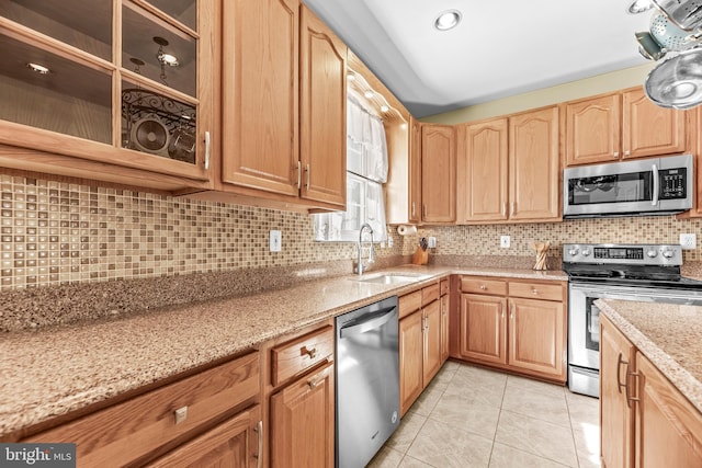 kitchen with stainless steel appliances, a sink, backsplash, light stone countertops, and light brown cabinets