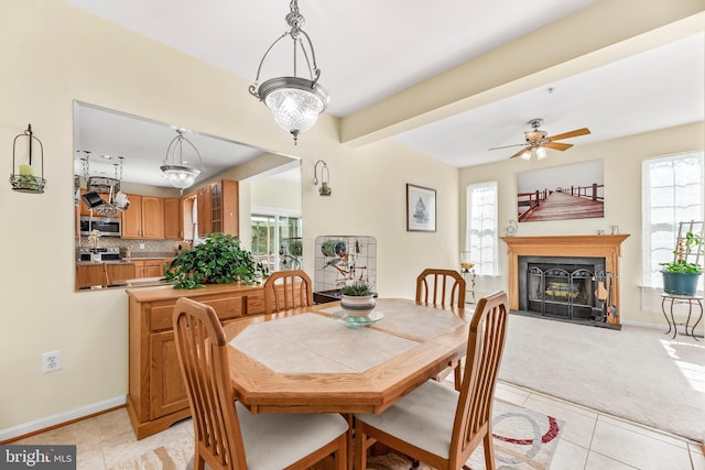 dining area with light tile patterned flooring, a fireplace with flush hearth, ceiling fan, and baseboards