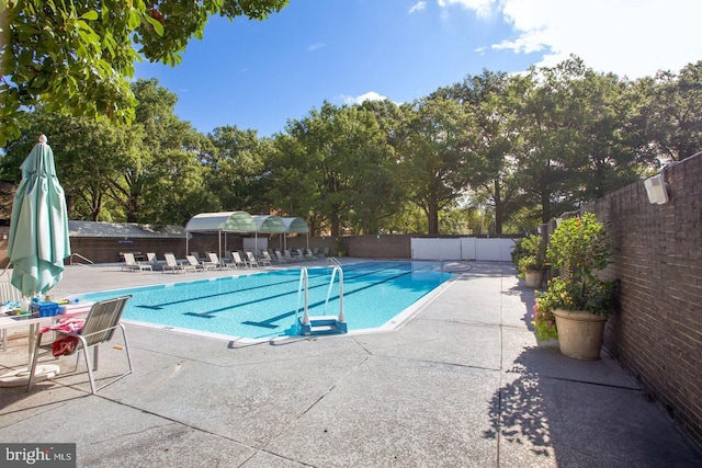 community pool with fence, a patio, and view of scattered trees