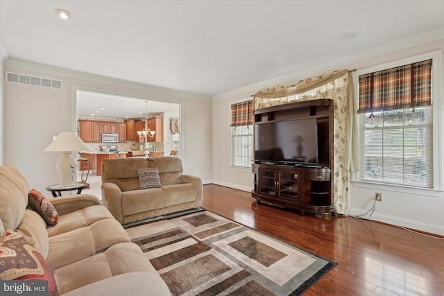 living room with baseboards, wood finished floors, ornamental molding, and a chandelier