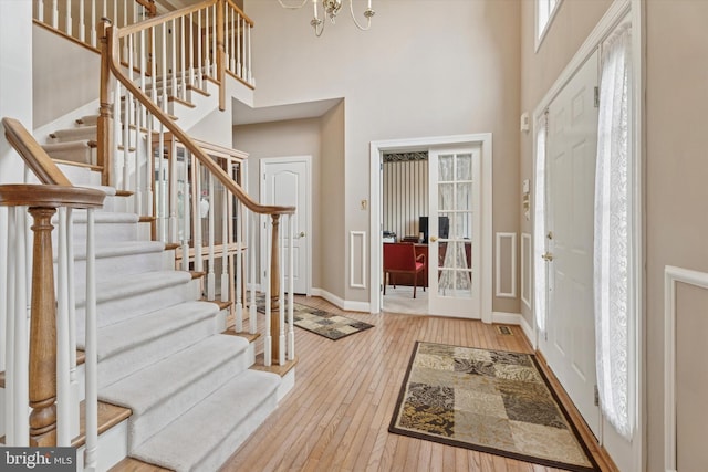 foyer entrance with a towering ceiling, stairs, wood-type flooring, baseboards, and a chandelier