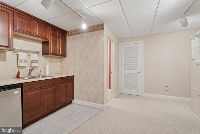 kitchen featuring a sink, dishwasher, light countertops, baseboards, and a paneled ceiling