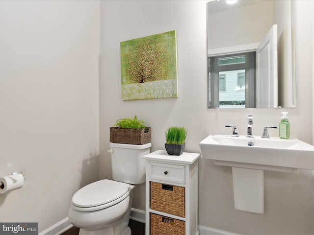 half bath featuring baseboards, toilet, and a sink