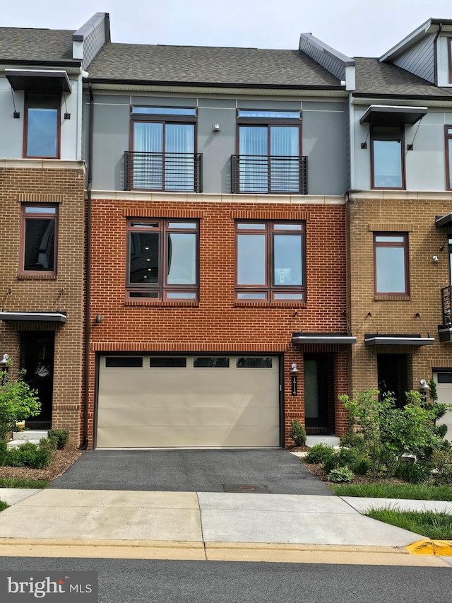 townhome / multi-family property featuring an attached garage, asphalt driveway, brick siding, and a shingled roof
