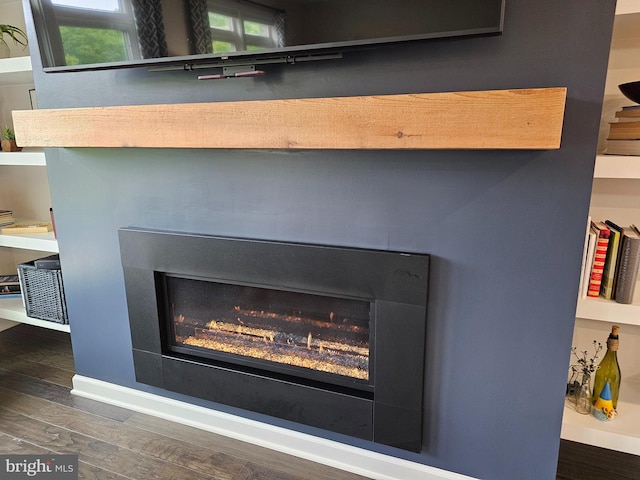 detailed view of a lit fireplace, wood finished floors, and baseboards