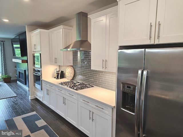kitchen with stainless steel appliances, wall chimney exhaust hood, white cabinetry, light countertops, and tasteful backsplash