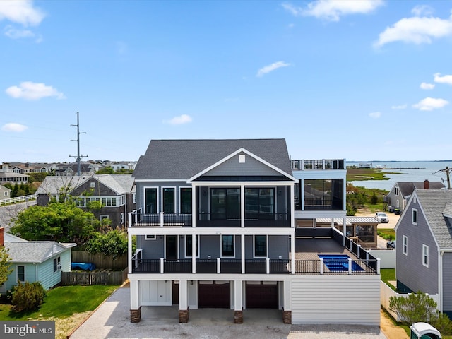 view of front facade featuring a balcony, a garage, a water view, driveway, and fence