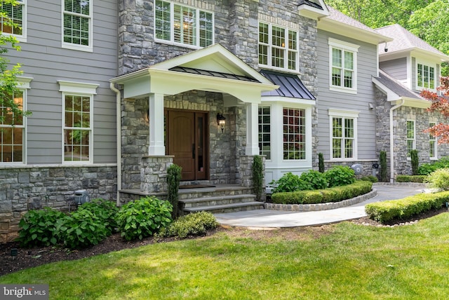 view of exterior entry with stone siding, a standing seam roof, and a lawn