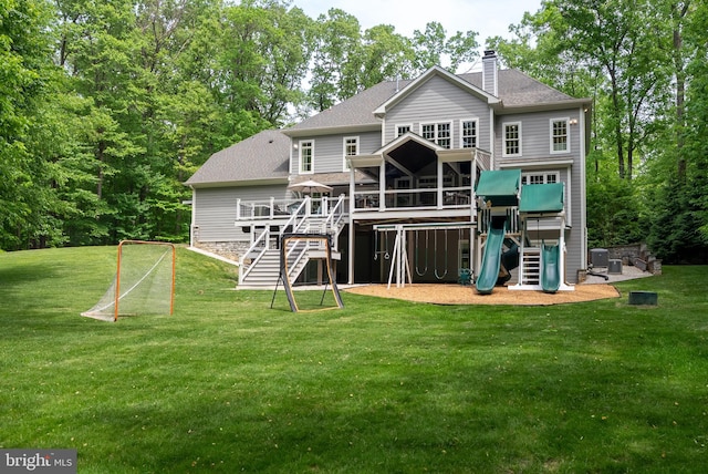 rear view of house featuring a chimney, a shingled roof, a deck, a playground, and a yard