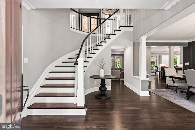 staircase with ornate columns, wood finished floors, ornamental molding, and baseboards