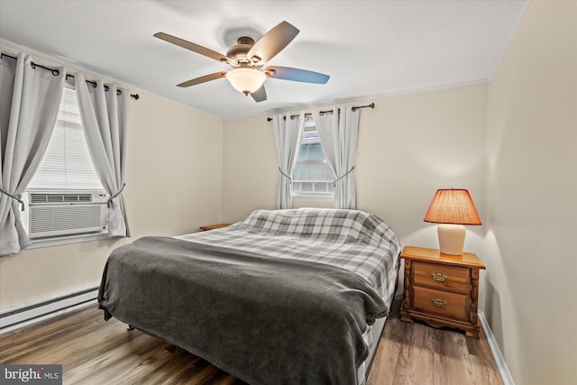 bedroom with baseboard heating, wood finished floors, baseboards, ornamental molding, and ceiling fan