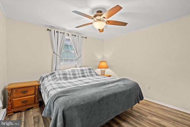 bedroom with baseboards, crown molding, wood finished floors, a baseboard heating unit, and a ceiling fan