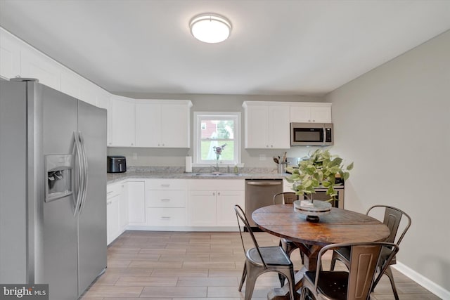 kitchen with stainless steel appliances, a sink, white cabinets, light stone counters, and light wood-type flooring