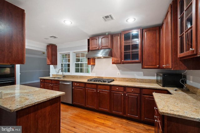 kitchen featuring black appliances, under cabinet range hood, a sink, light stone counters, and glass insert cabinets