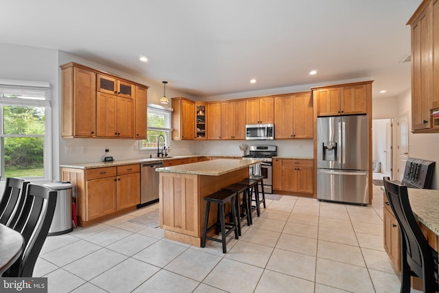 kitchen featuring stainless steel appliances, recessed lighting, a kitchen island, brown cabinets, and light stone counters