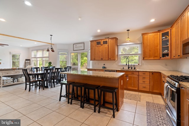 kitchen featuring appliances with stainless steel finishes, a sink, brown cabinets, light stone countertops, and plenty of natural light