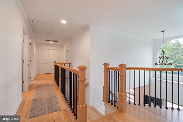 hall with an upstairs landing, attic access, a chandelier, wood finished floors, and ornamental molding