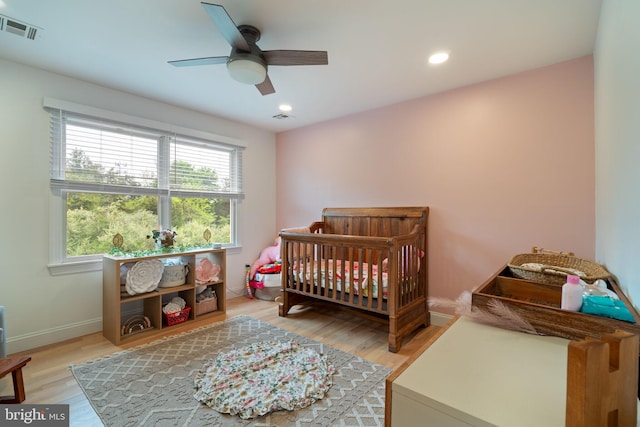 bedroom featuring light wood-type flooring, a ceiling fan, recessed lighting, a crib, and baseboards